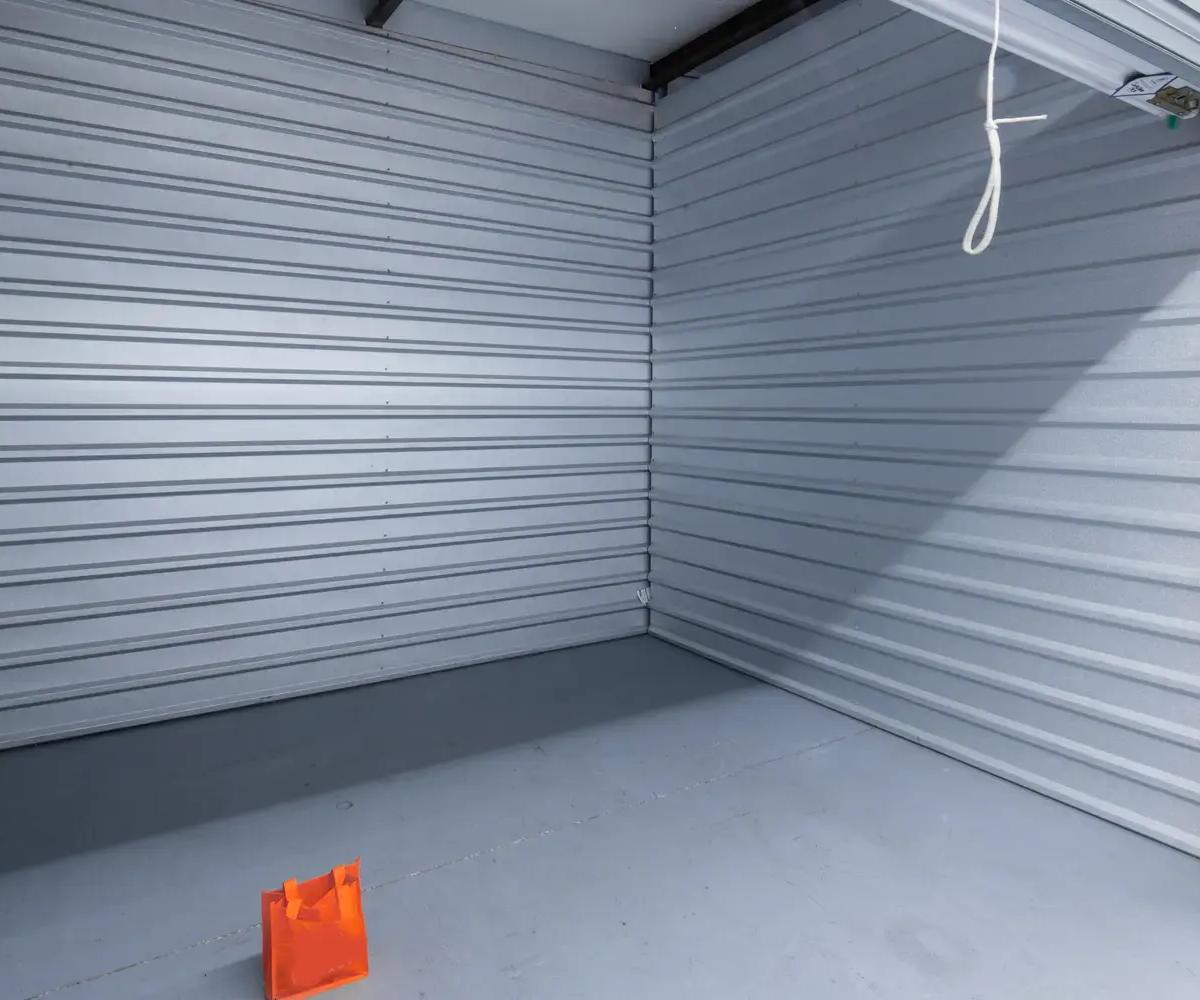 Interior view of an empty storage unit with corrugated metal walls and an orange bag on the floor