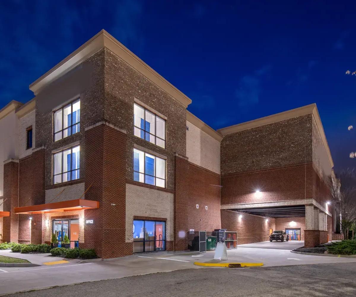 A multi-story brick storage facility at night featuring an office entrance and a covered loading bay