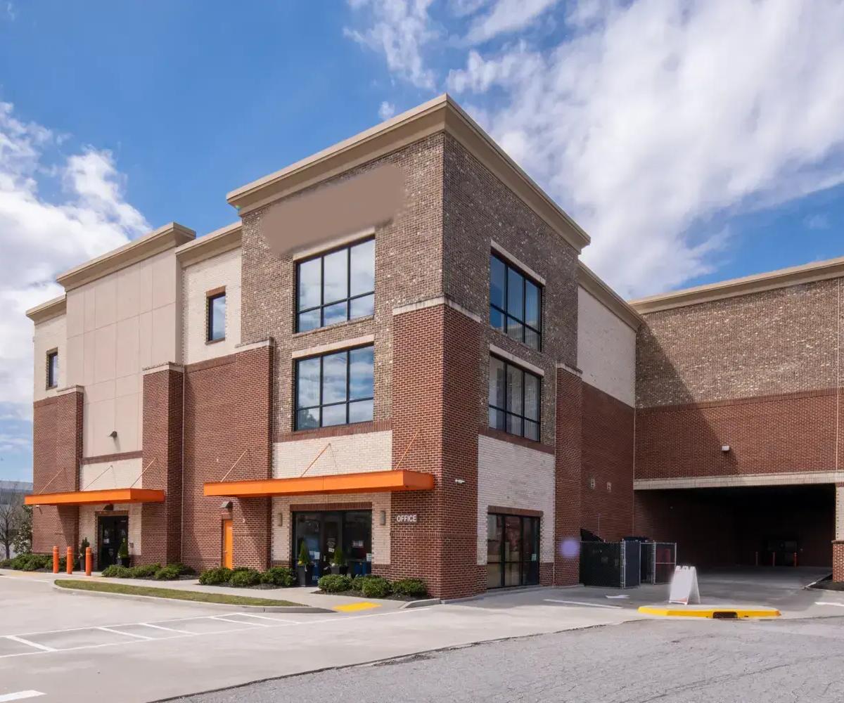 Exterior view of a multi-story brick storage facility office with orange awnings and a paved parking lot