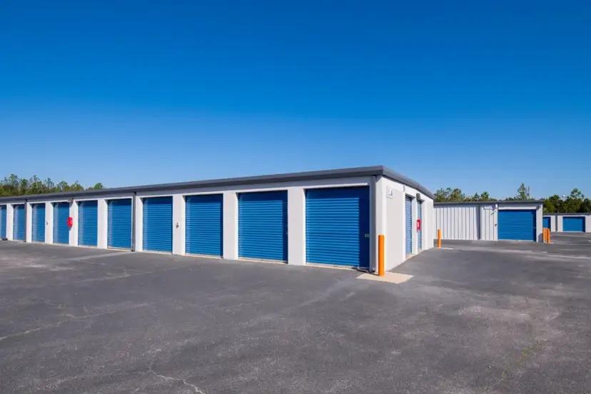 Rows of outdoor drive-up storage units with blue roll-up doors under a clear sky
