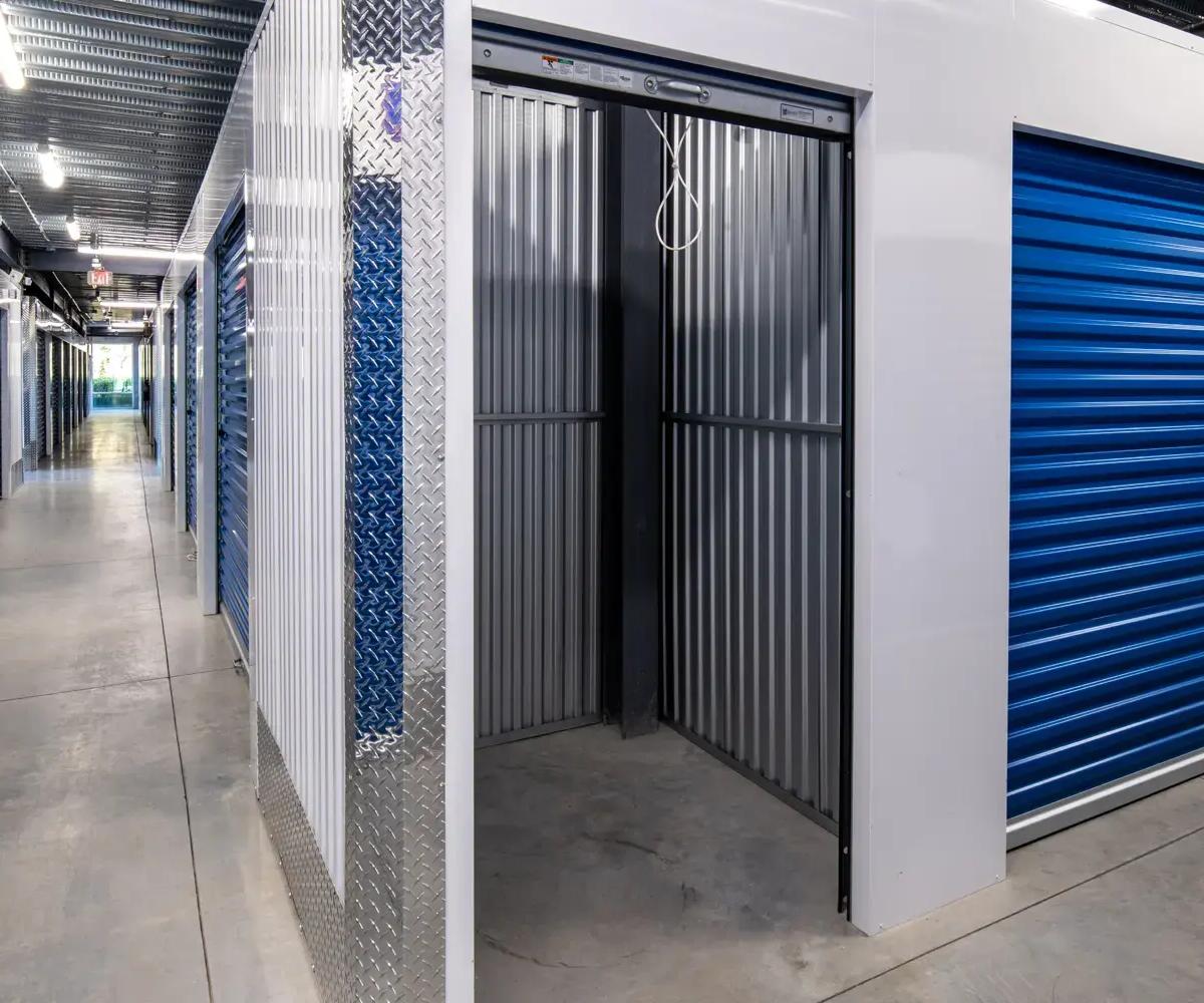 Indoor storage facility hallway with an open unit showing corrugated metal walls and blue roll-up doors
