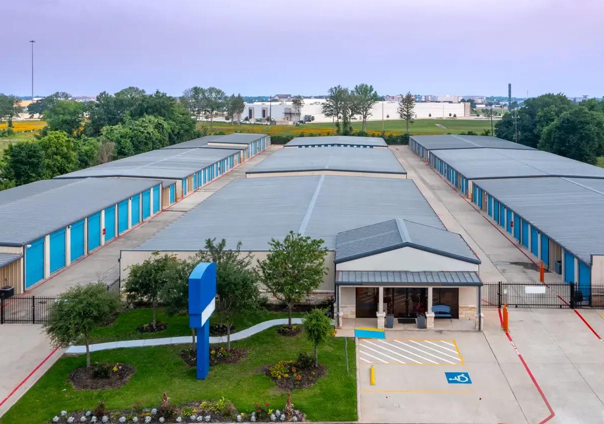 An aerial view of a self-storage facility featuring rows of blue units and an office building