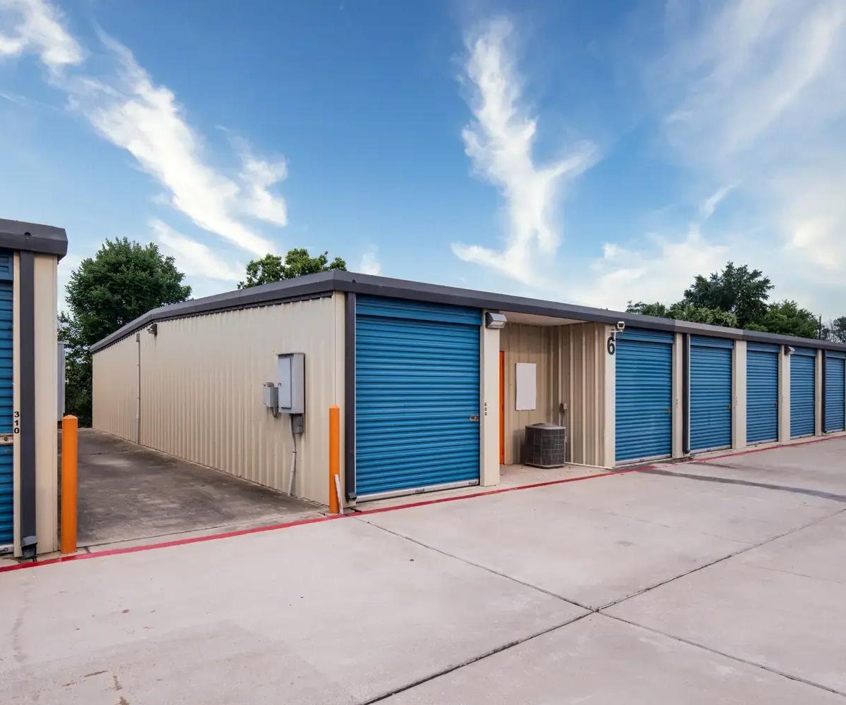 Outdoor drive-up self-storage facility with tan metal siding and blue roll-up unit doors along a concrete path
