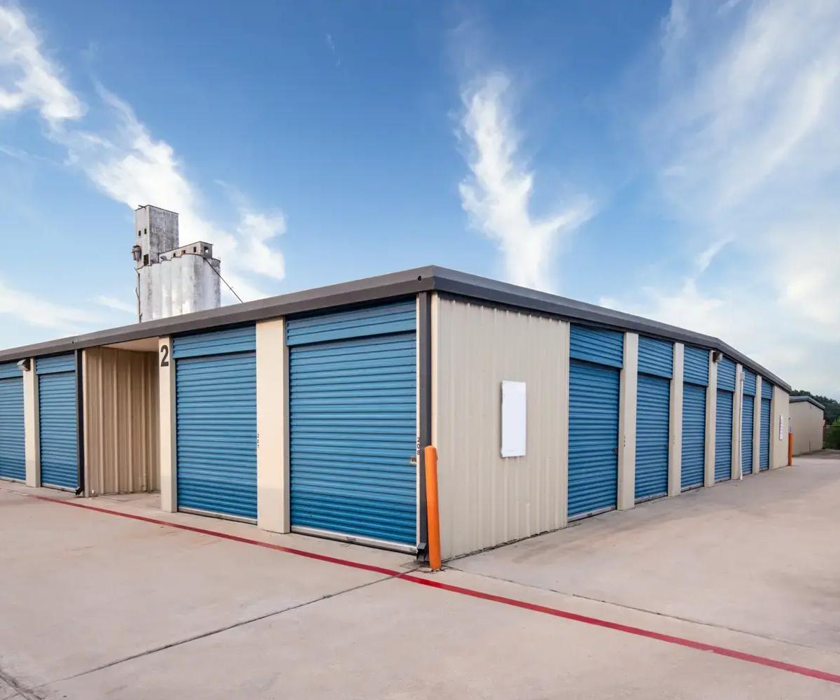 Exterior view of a self-storage building with blue roll-up doors and a concrete drive-up aisle