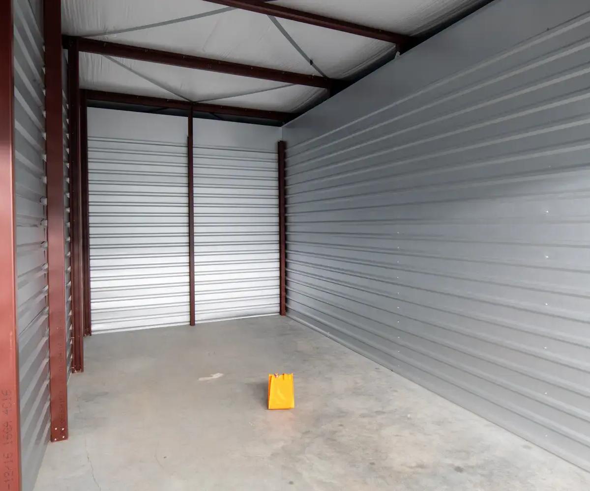 An empty drive-up self-storage unit featuring corrugated metal walls, a concrete floor, and high ceilings