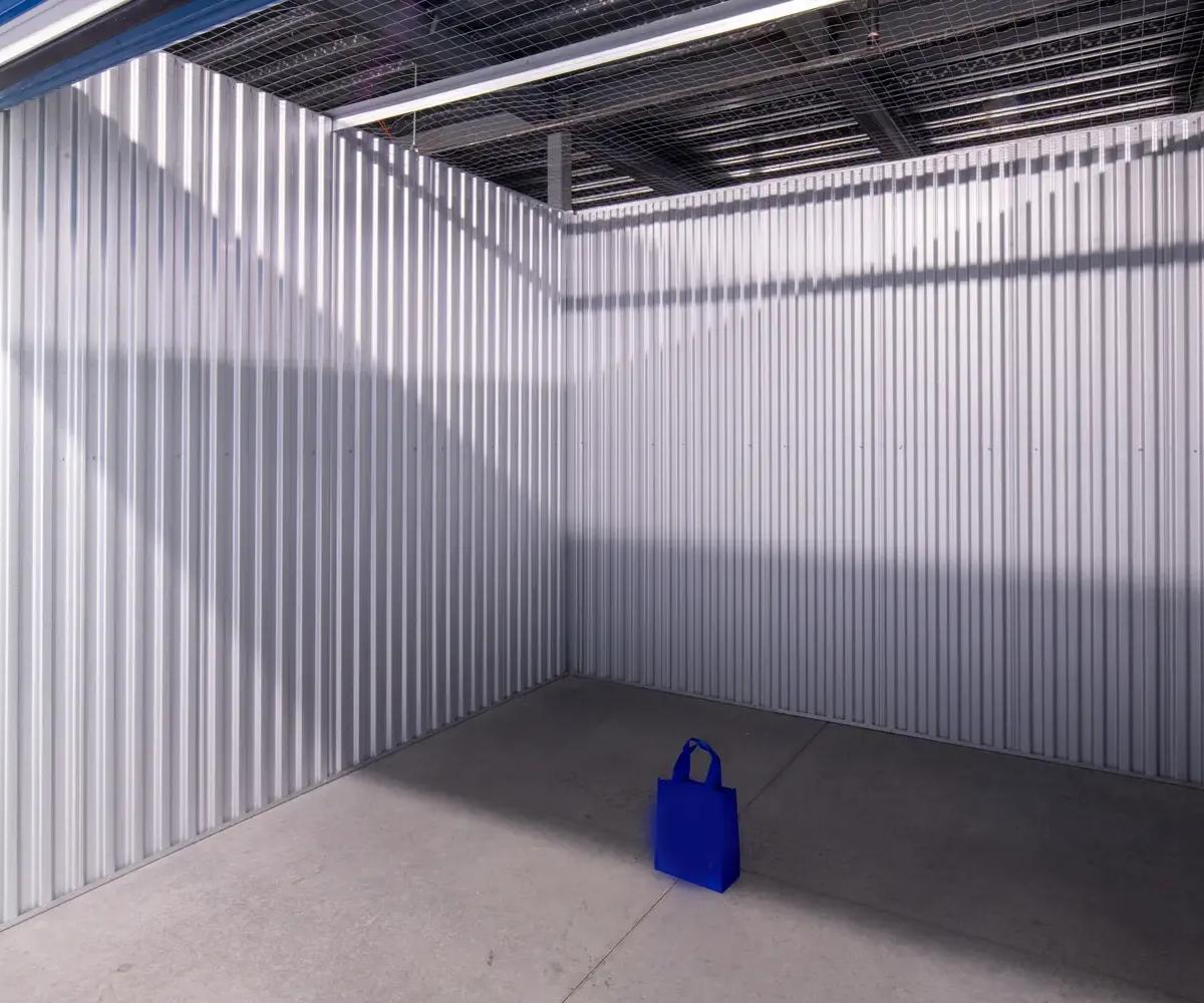 Interior view of an empty storage unit with corrugated metal walls and a single blue bag