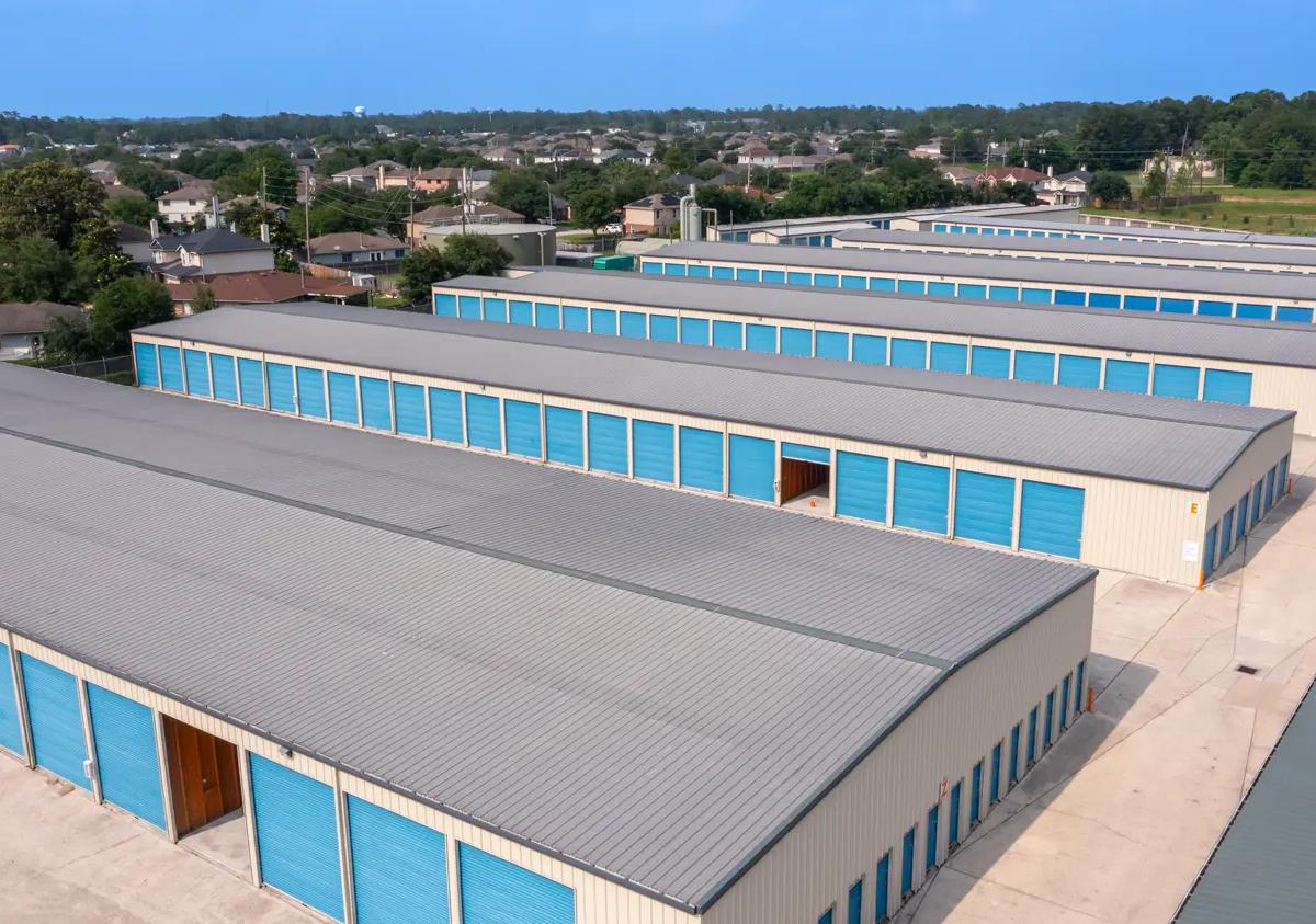Aerial view of long rows of drive-up storage buildings with blue roll-up doors and gray metal roofs
