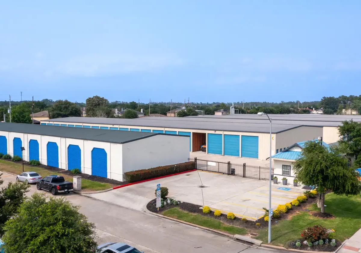 Aerial view of a self-storage facility with gated access, blue roll-up doors, and parked vehicles