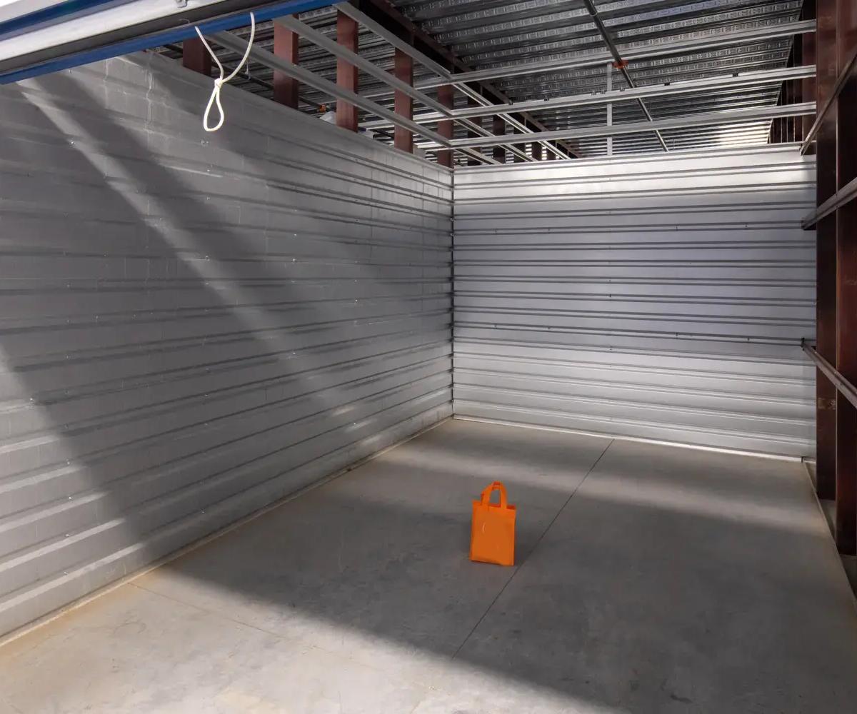 An empty indoor storage unit with corrugated metal walls and a single orange bag on the floor