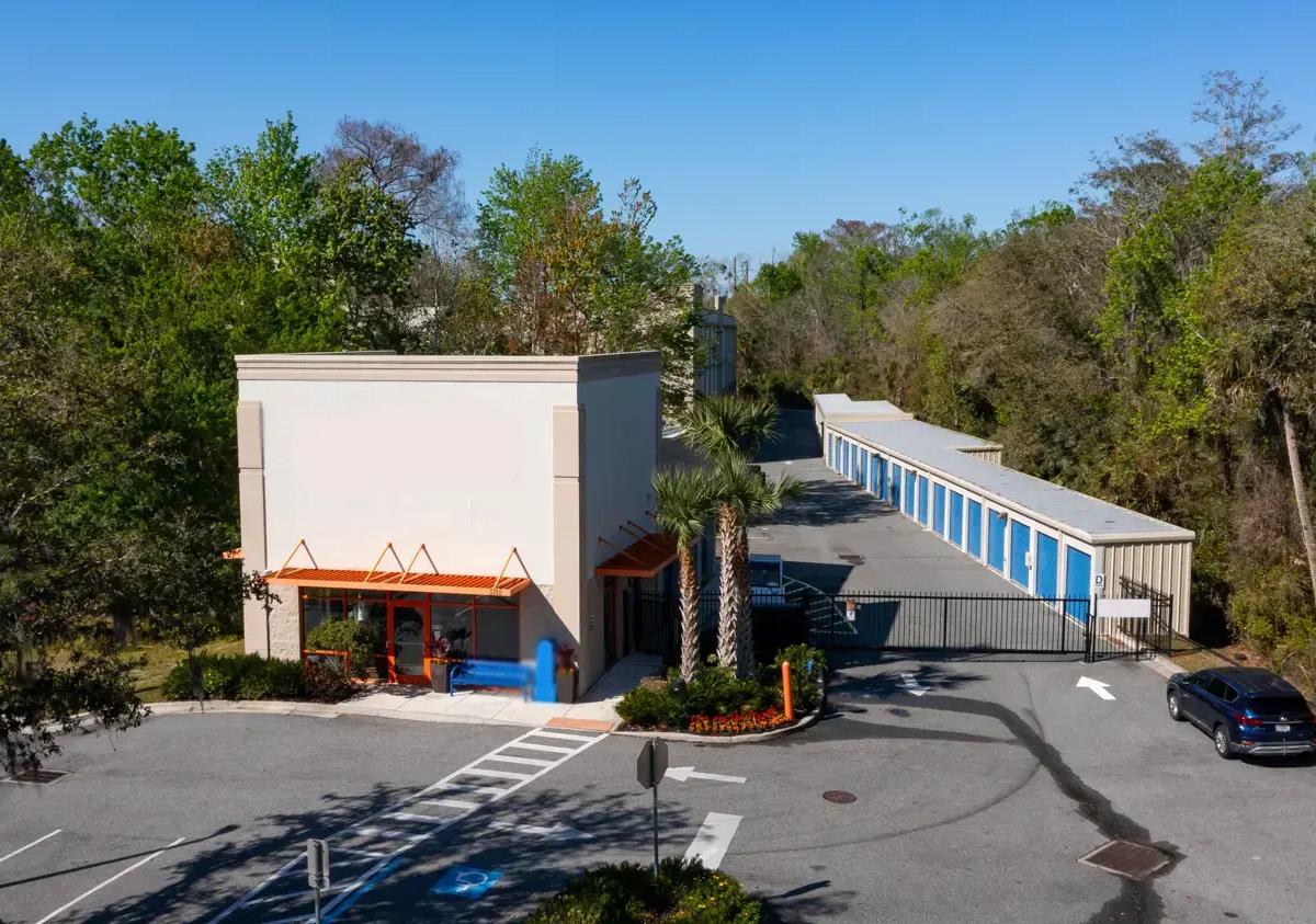 Aerial view of a storage rental office and gated drive-up units with blue roll-up doors
