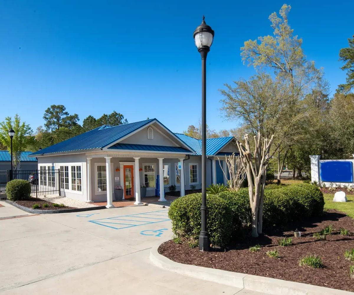A storage rental office building with a blue metal roof, orange door, and lamp post
