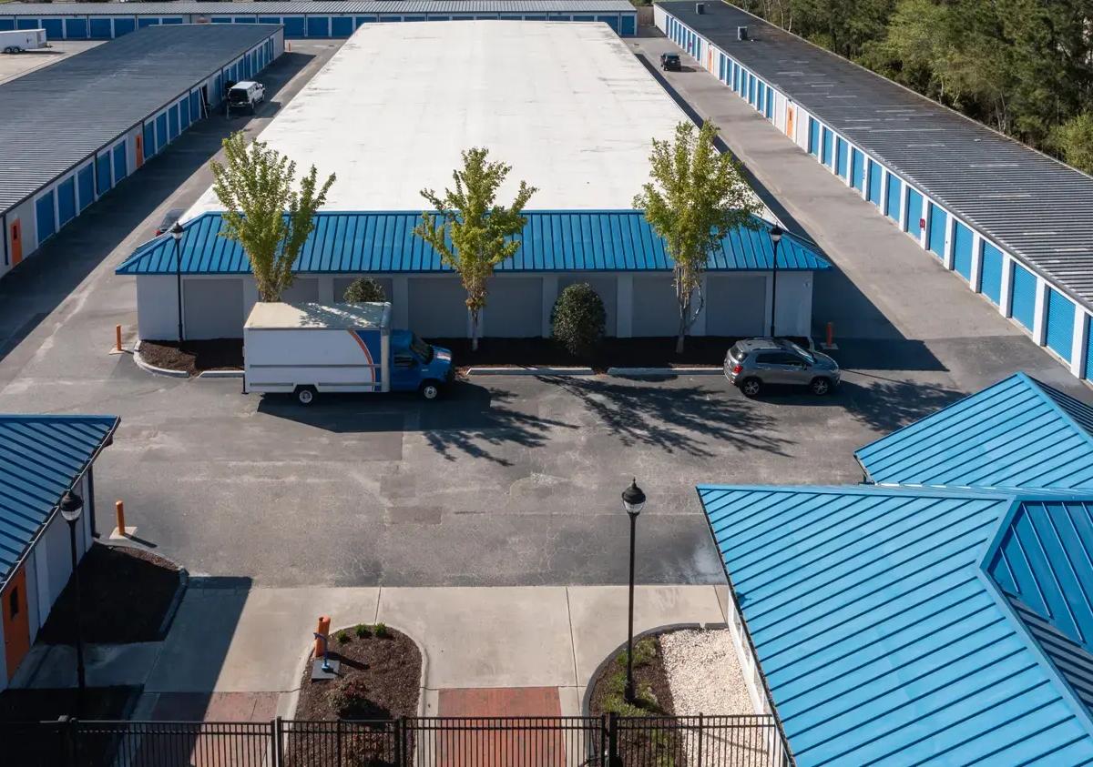Aerial view of storage buildings with blue roofs and a moving truck parked in the paved lot