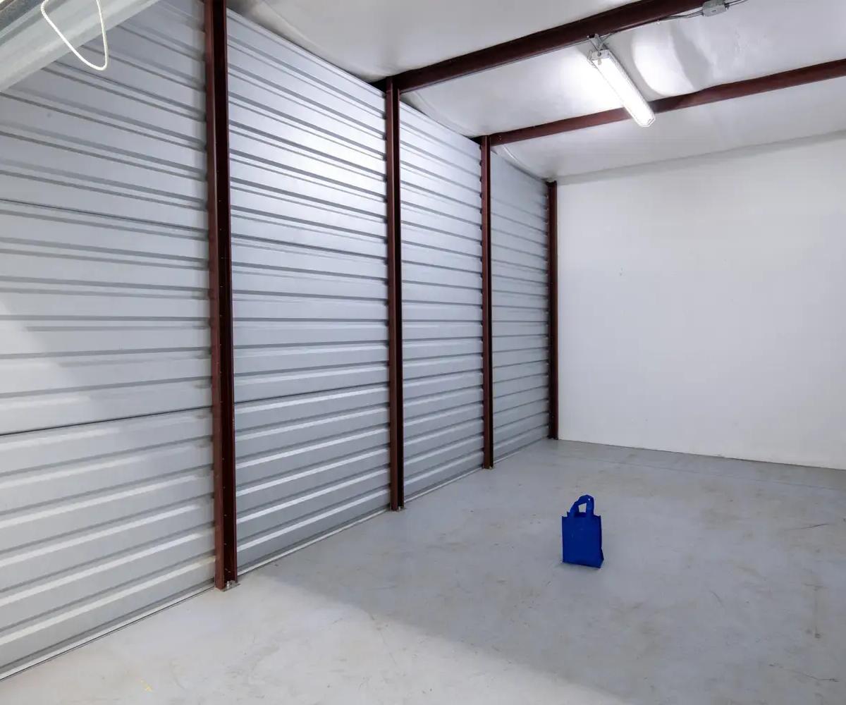 Interior of a large empty storage unit with corrugated metal walls and a single blue bag