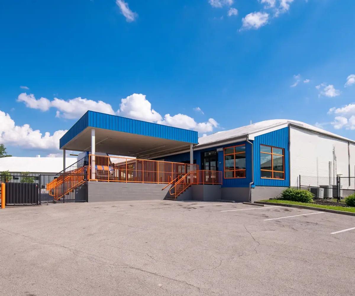 Blue storage facility office with a covered loading dock, orange railings, and a paved parking lot
