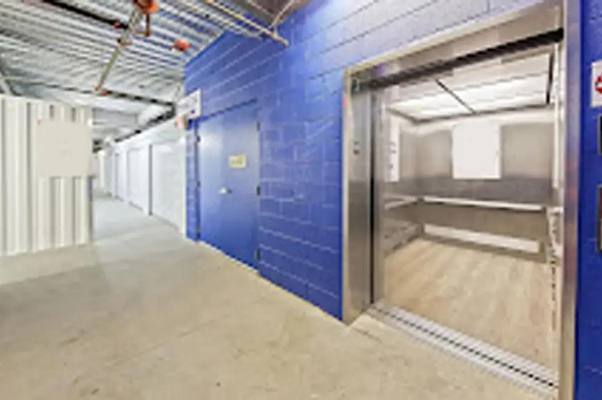 Indoor storage unit hallway with a blue brick wall next to an open freight elevator door