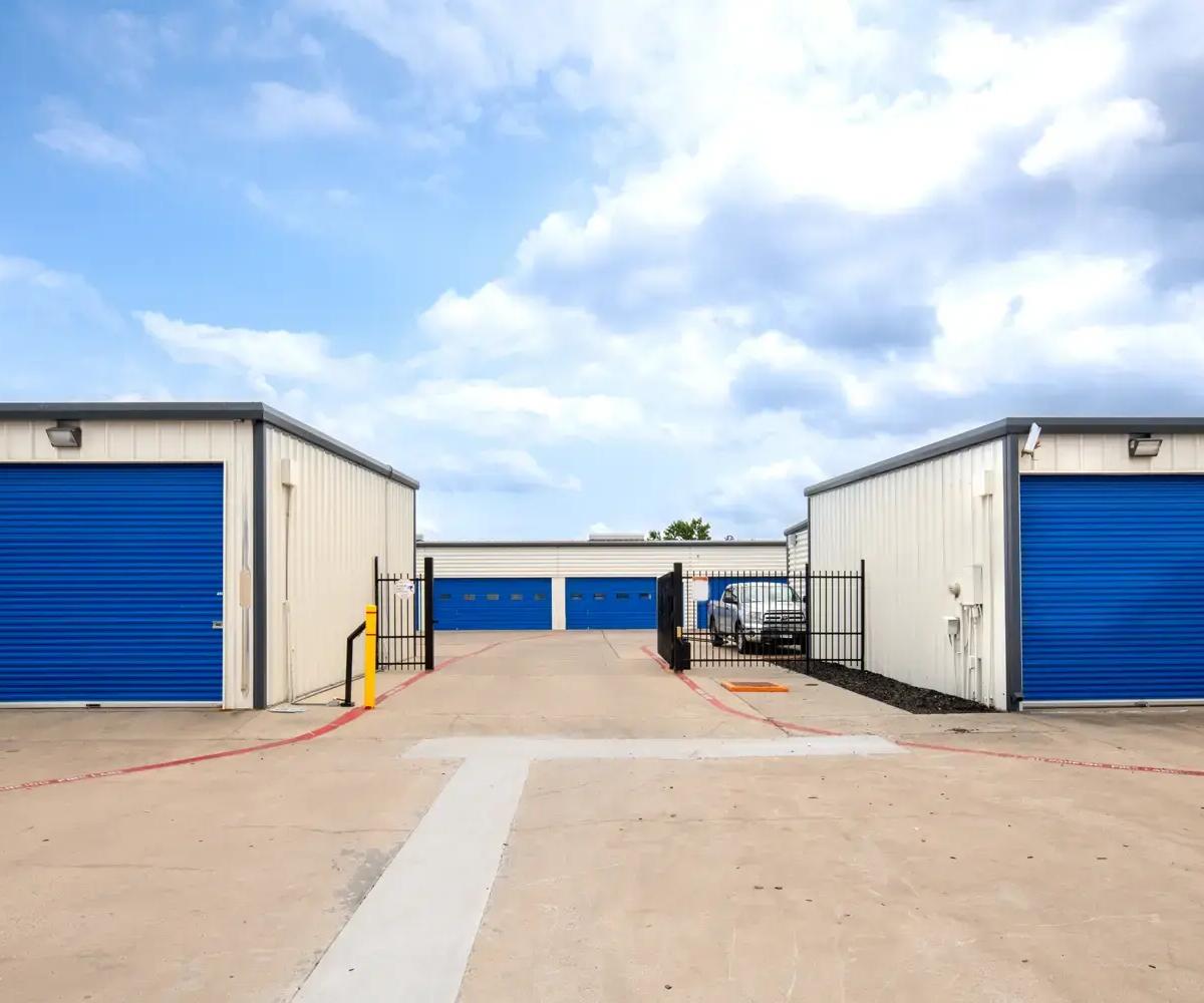 Drive-up self-storage buildings with blue roll-up doors and an open black metal security gate